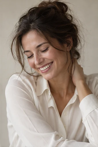 A brunette woman smiles with her eyes lowered, wearing an ivory collared shirt.